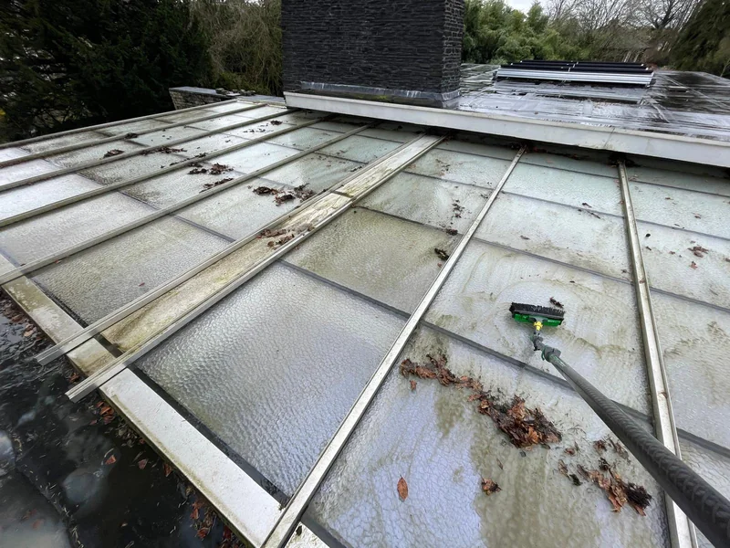 Leaves and dirt on a glass roof, with a brush beside the panels