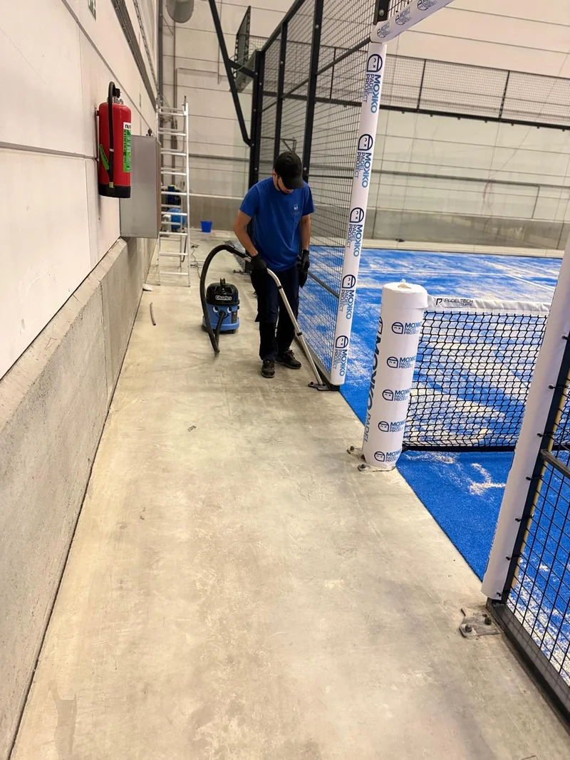 Worker vacuuming the walkway beside an indoor padel court